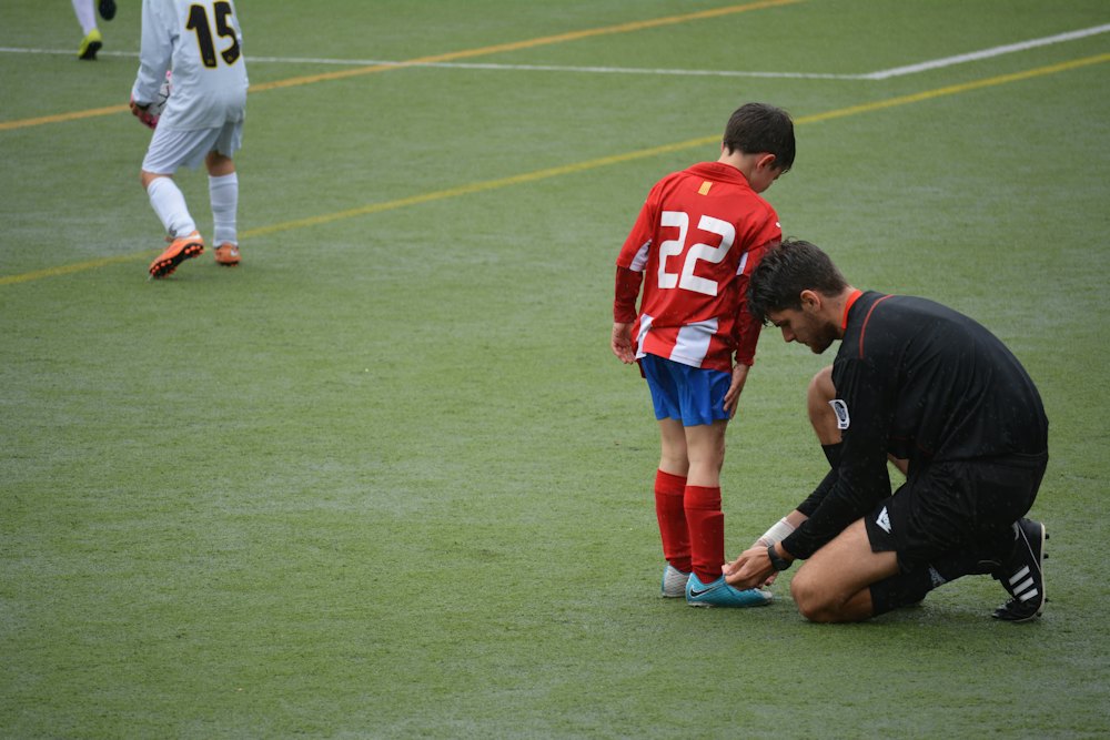 Un entrenador le ata los botines a un chico en la cancha