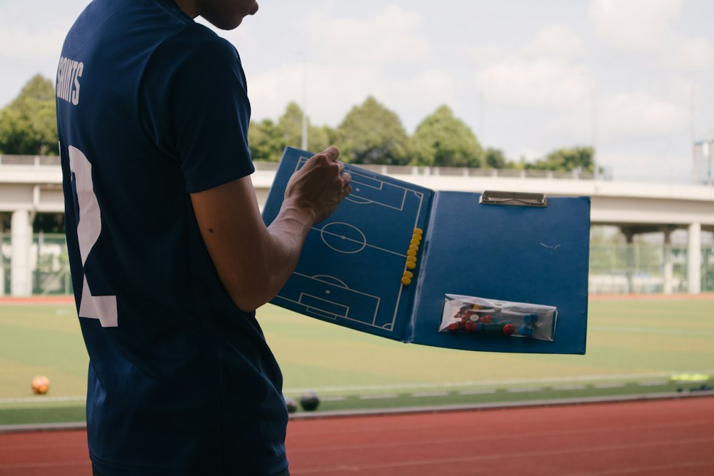 Un entrenador con la carpeta táctica abierta al costado de la cancha